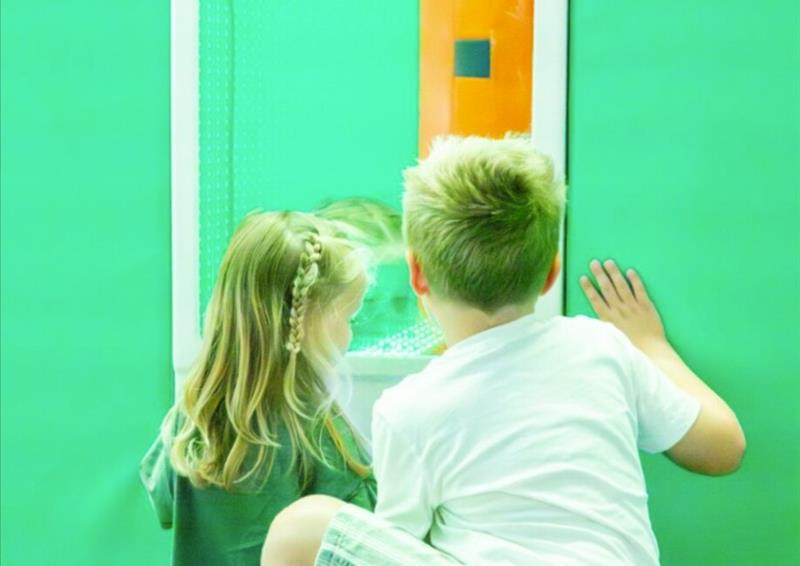 Two children looking at a brightly coloured panel on a green wall